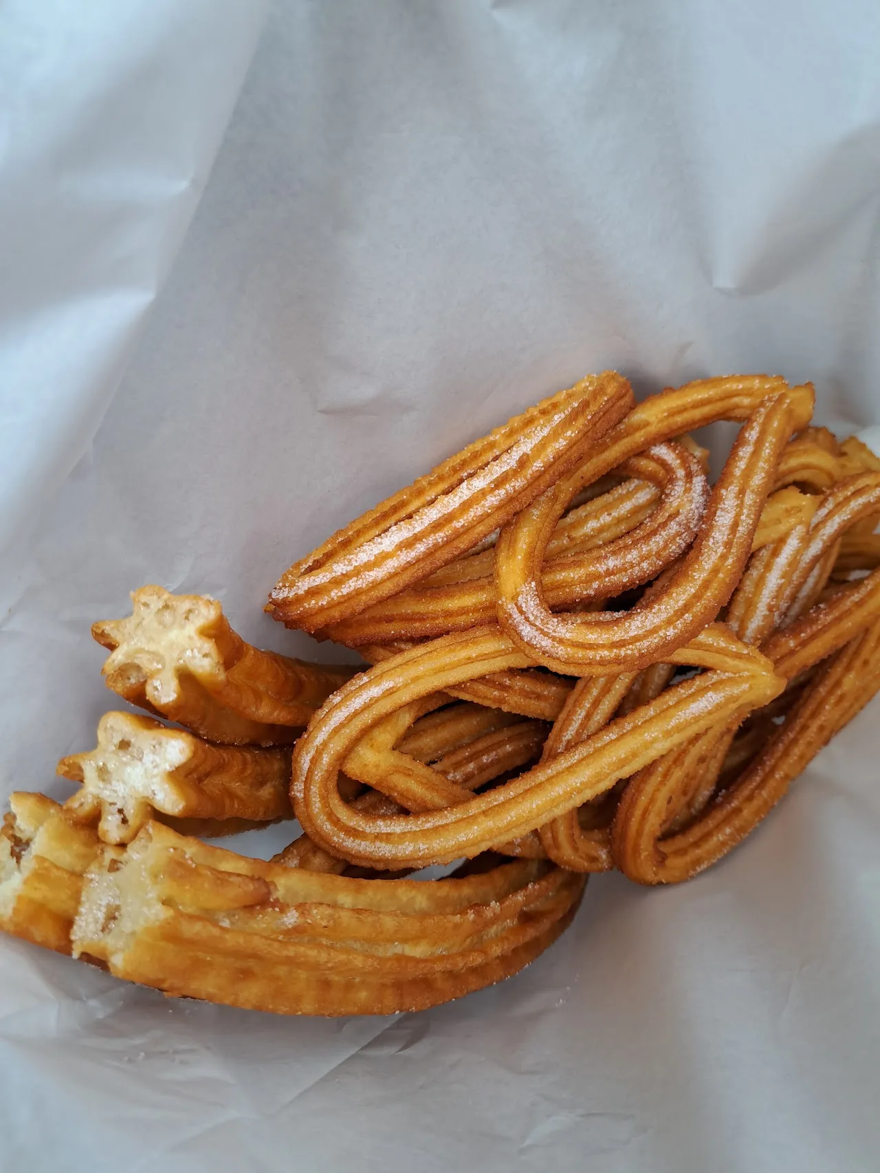 Churros wrapped in white paper, held close up