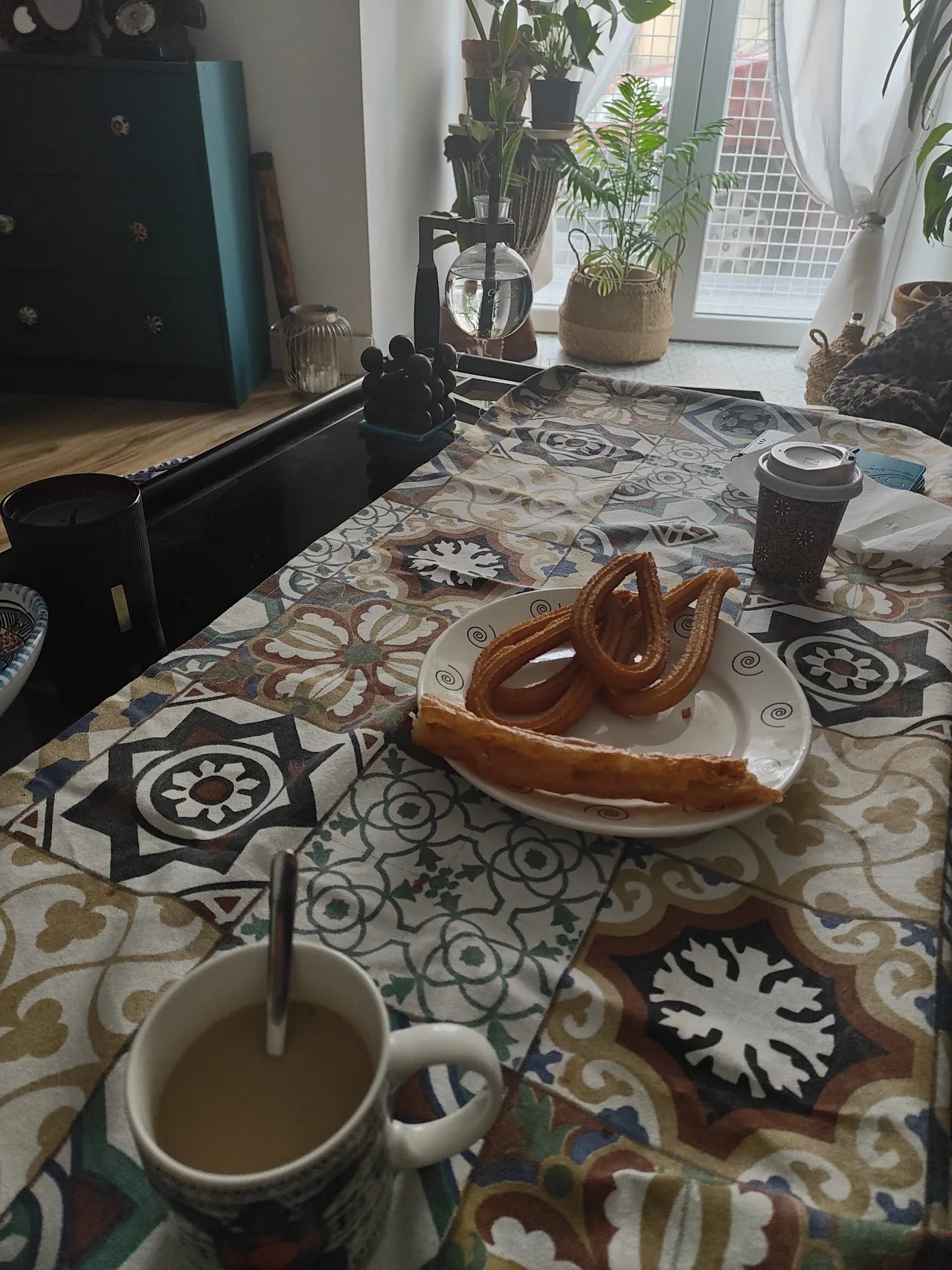 A table set with churros, cups of hot chocolate, and drinks on a decorative tiled table