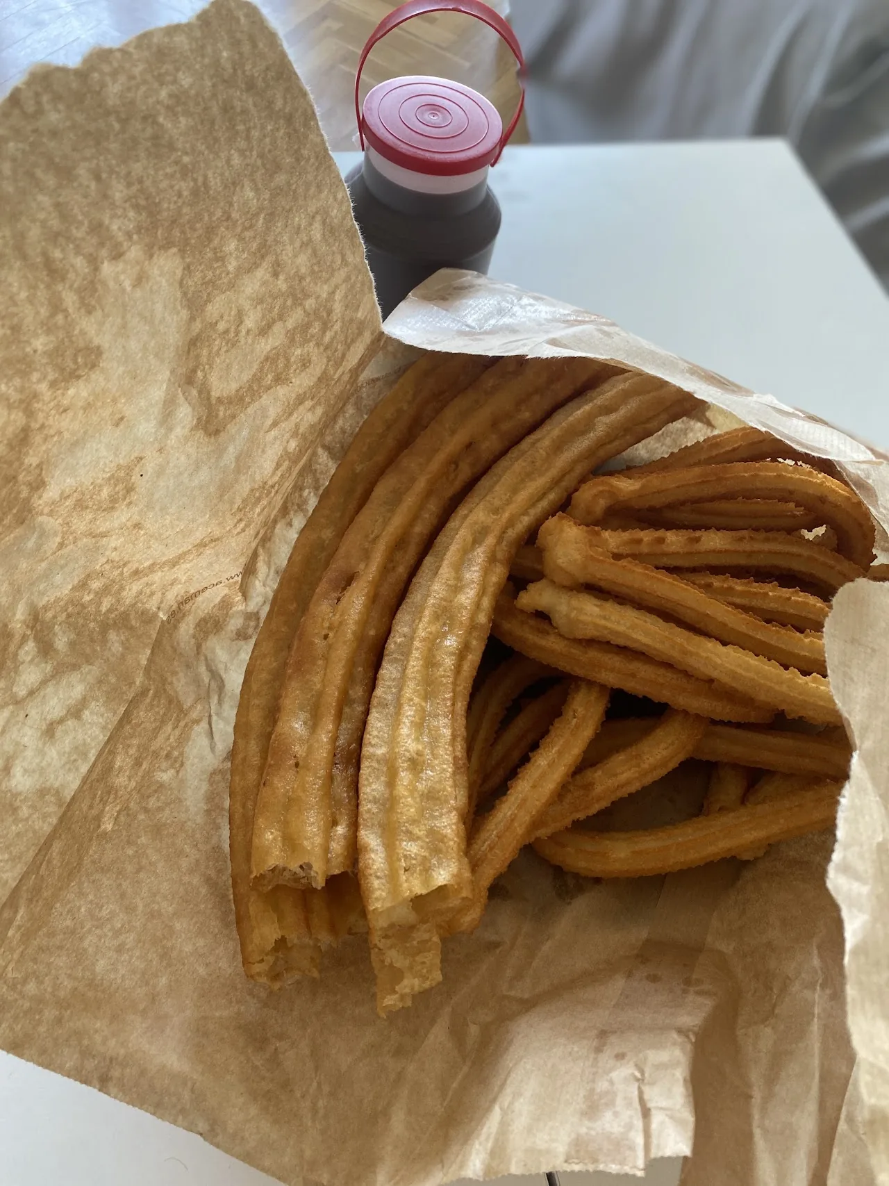A paper bag of churros beside a small pot of sauce