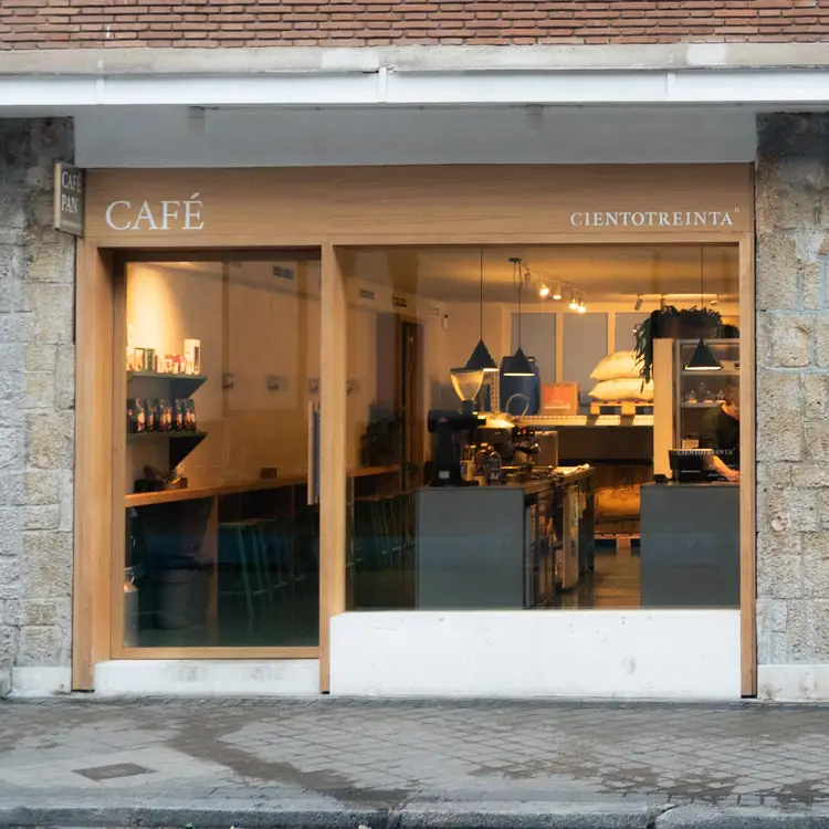 Street exterior of Cafe Cientotreinta, a wood-framed window front with 'CAFE' and 'CIENTOTREINTA' lettering and the coffee counter glowing inside