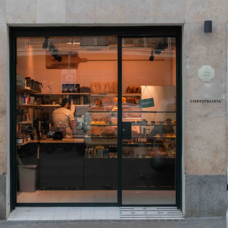 Storefront window of Cientotreinta with a green 'ABIERTO' sign, bakery counter and shelves of bread visible through the glass, 'CIENTOTREINTA' engraved on the stone