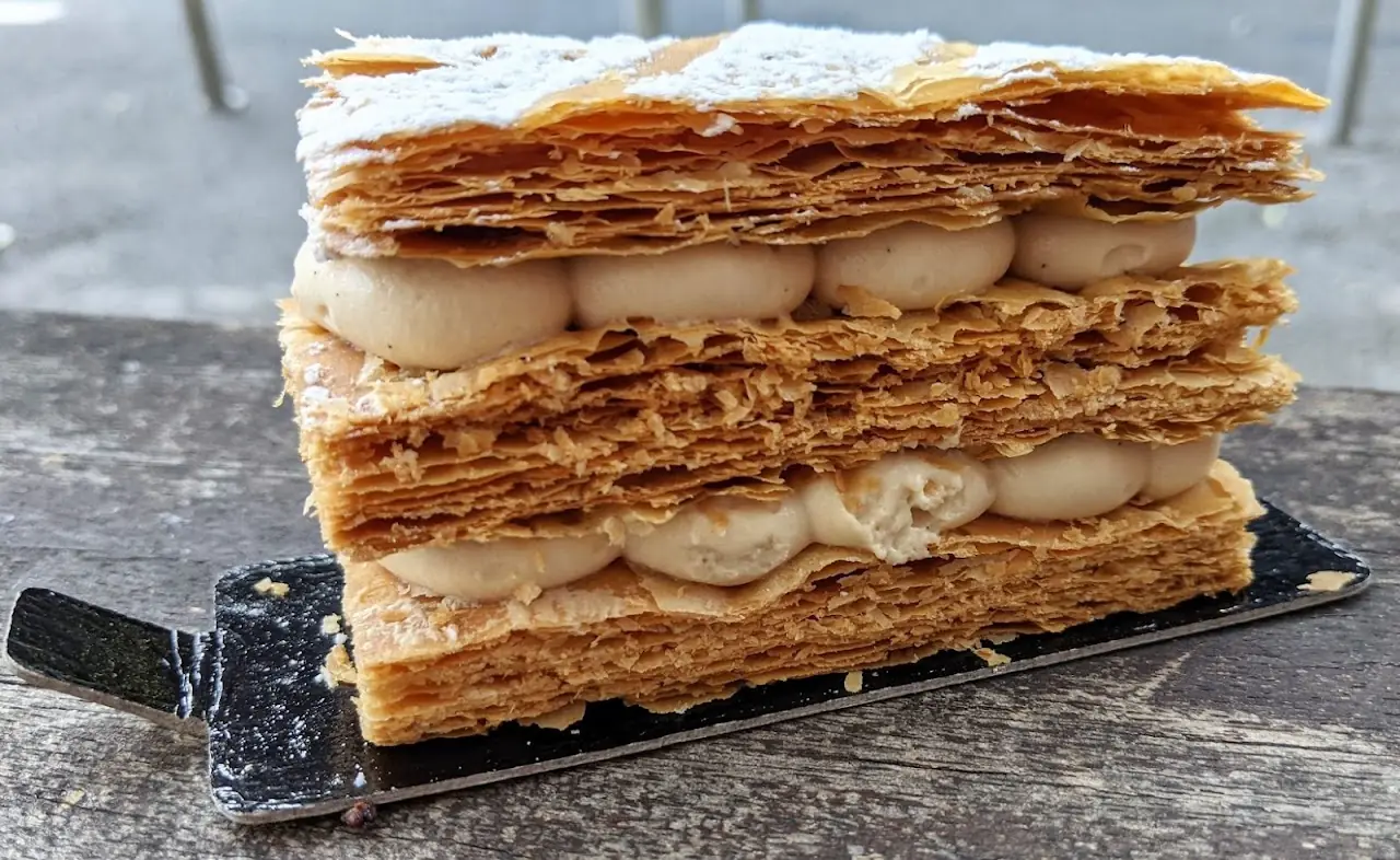 A cross-section of a layered mille-feuille pastry with cream filling, dusted with powdered sugar