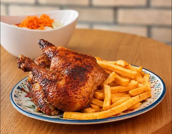 Roasted half chicken with golden fries and a bowl of grated carrot salad on a patterned plate