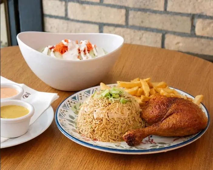 Roast chicken leg with brown rice, fries, salad bowl and two dipping sauces on a table