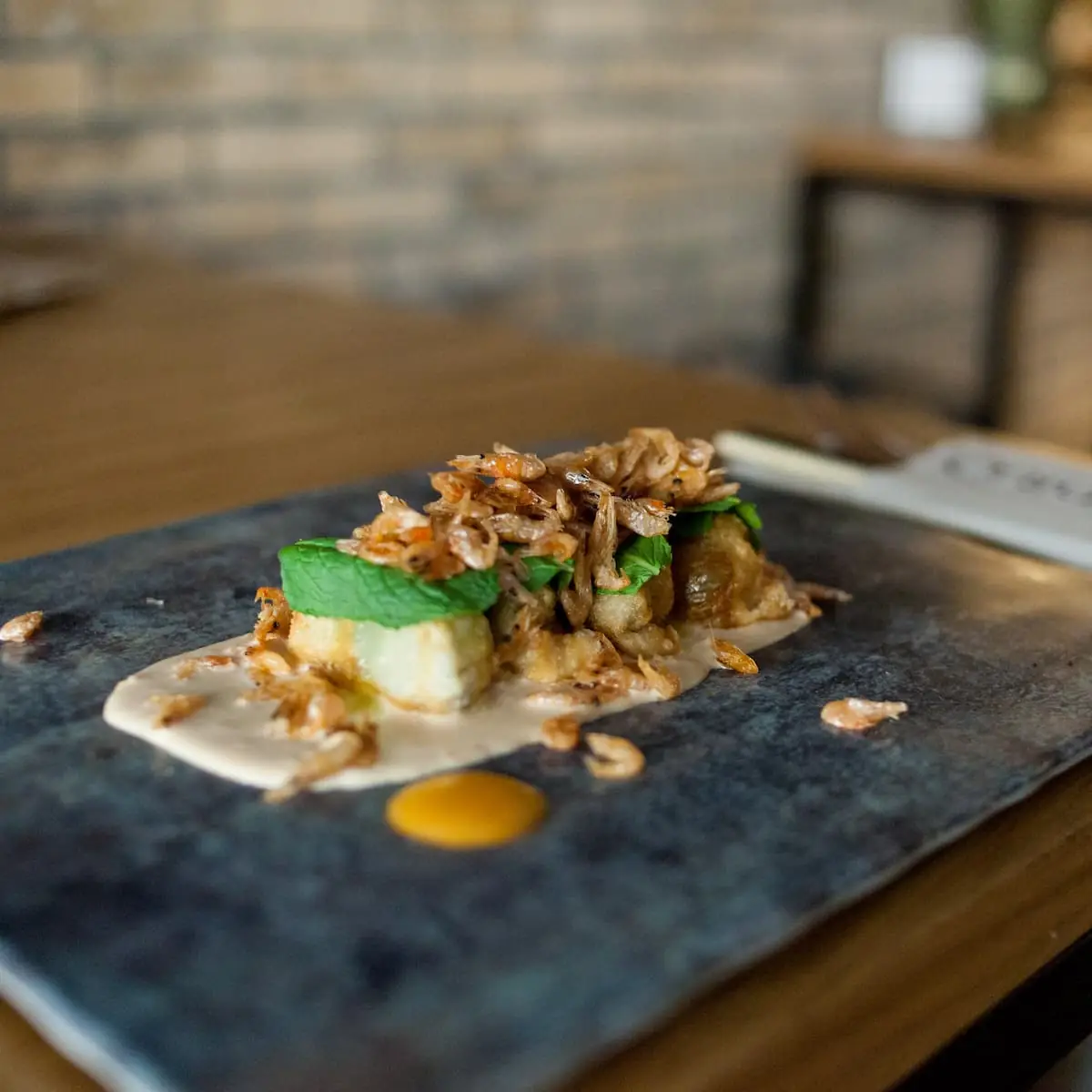 Plated dish of fried baby shrimp and mint over a cube in cream sauce on a slate board