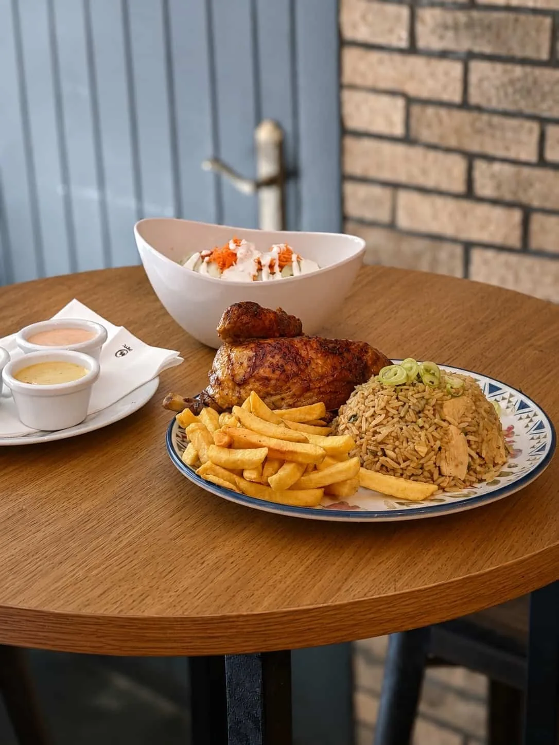 A plate with roast chicken, fried rice and french fries next to a bowl of salad and dipping sauces