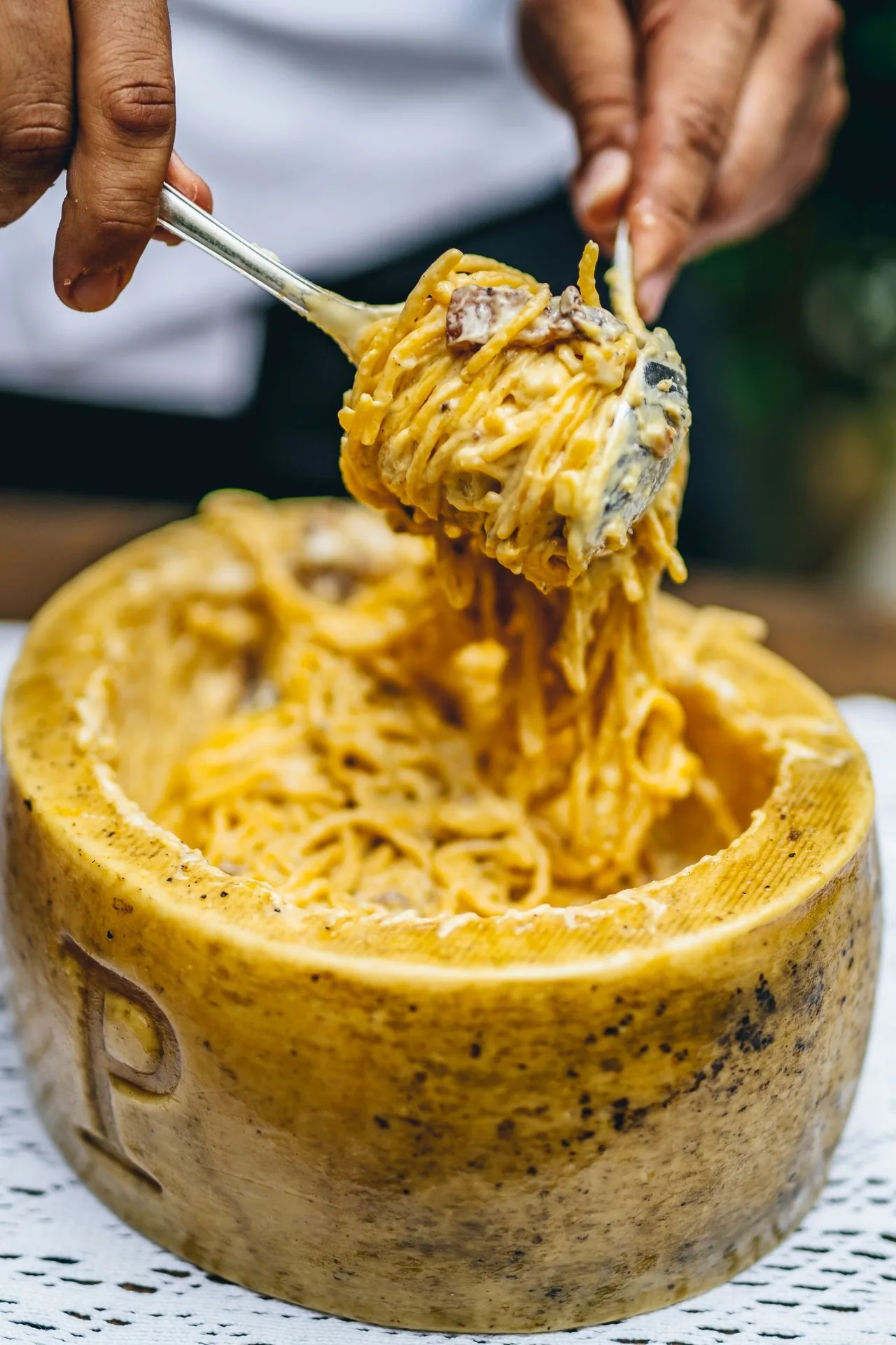 Spaghetti being lifted with a fork from a hollowed round of hard cheese