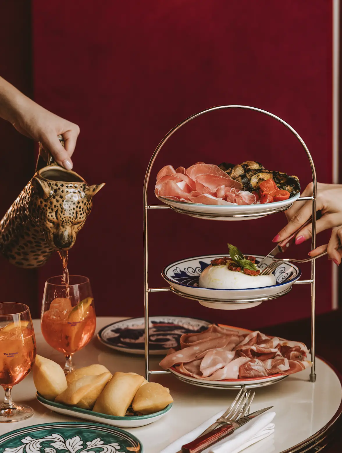 A tiered stand of cured meats, olives, and burrata being served, with a cocktail alongside.