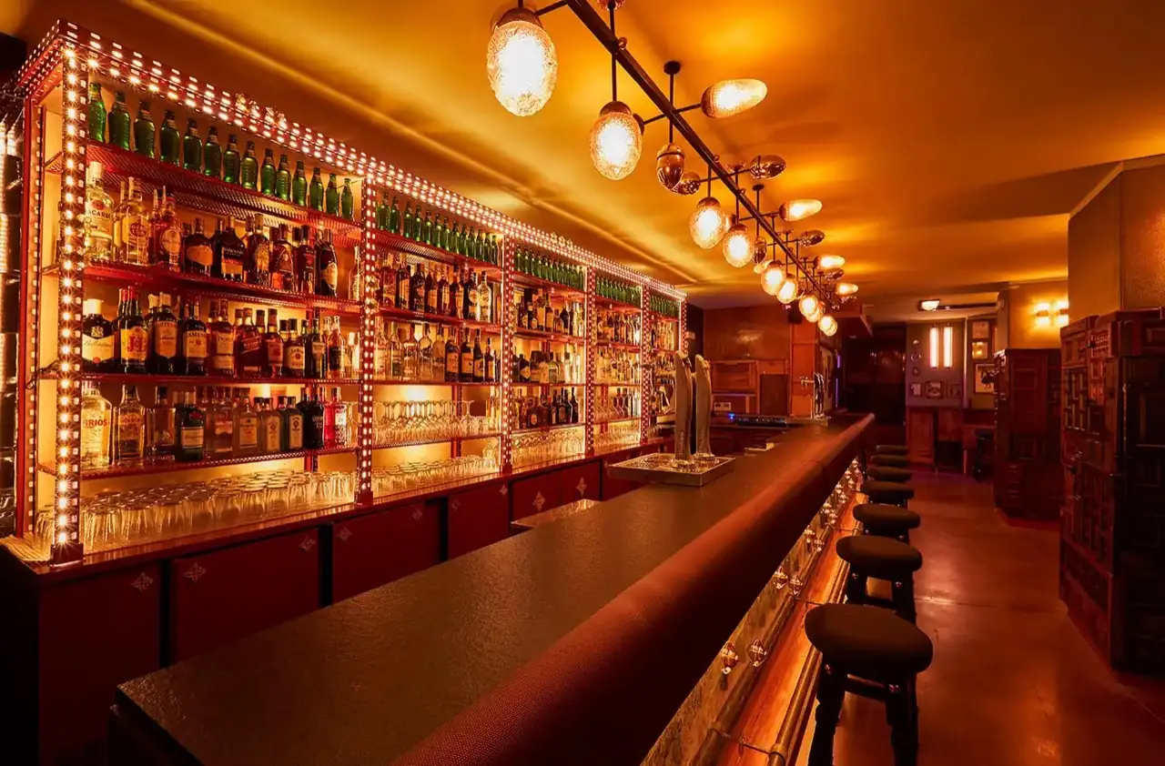 Length of the bar counter with illuminated bottle shelving, cluster of glass pendant lights and a row of stools