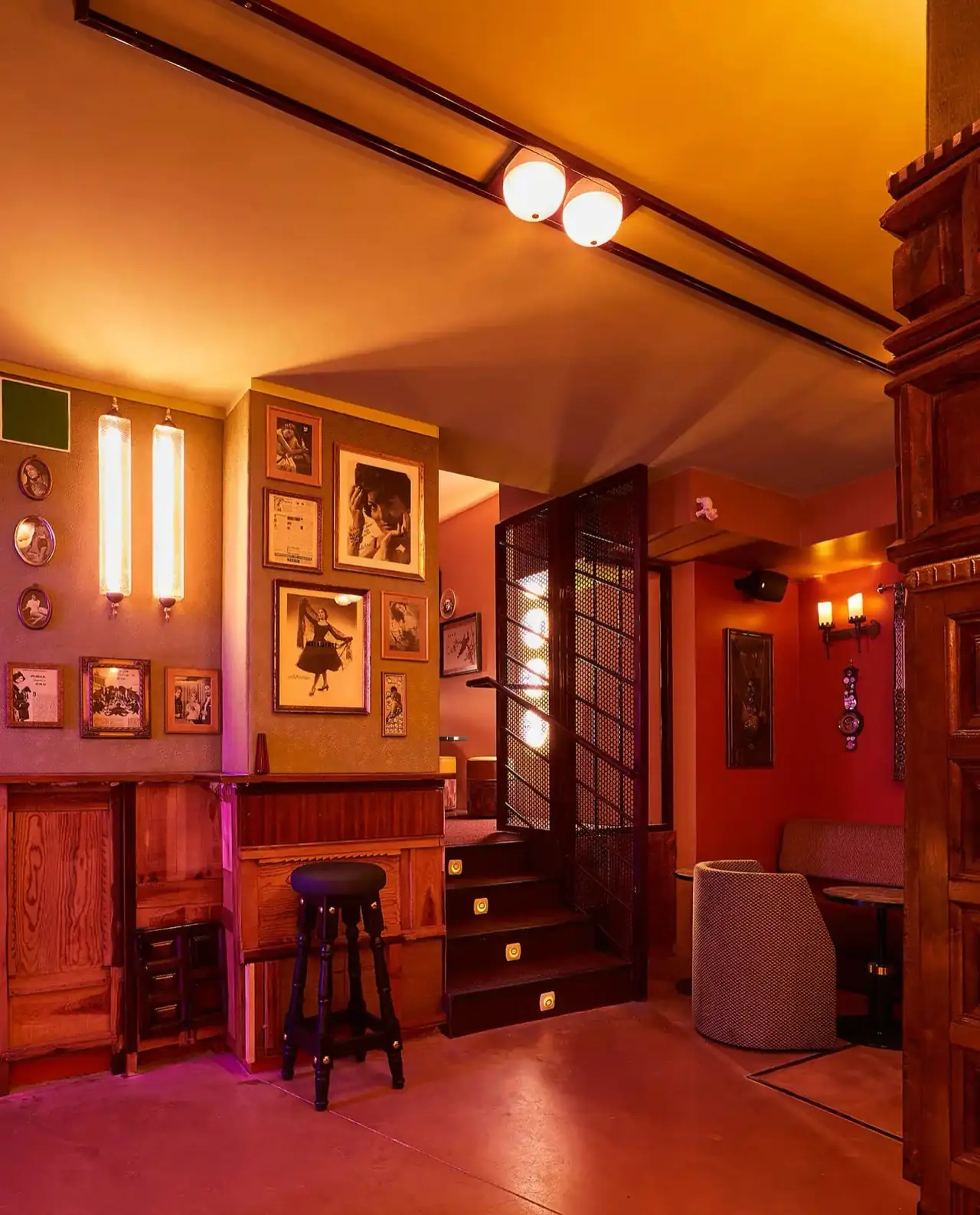 Interior corner with a gallery wall of framed black-and-white photos, a stool, a metal-caged staircase and a seating nook