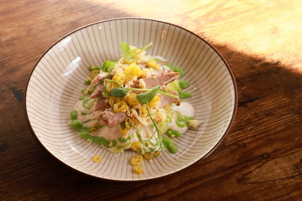 Sliced tuna with pickled yellow peppers, grated egg, pea-cream drizzle and microgreens in a striped bowl on a wooden table