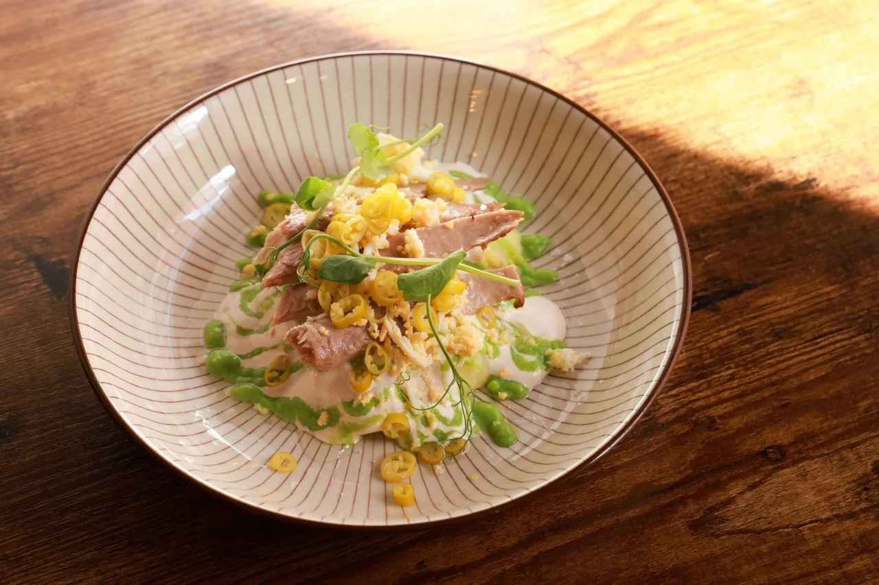 A striped bowl of shredded fish and vegetables with corn and green pepper on a wooden table