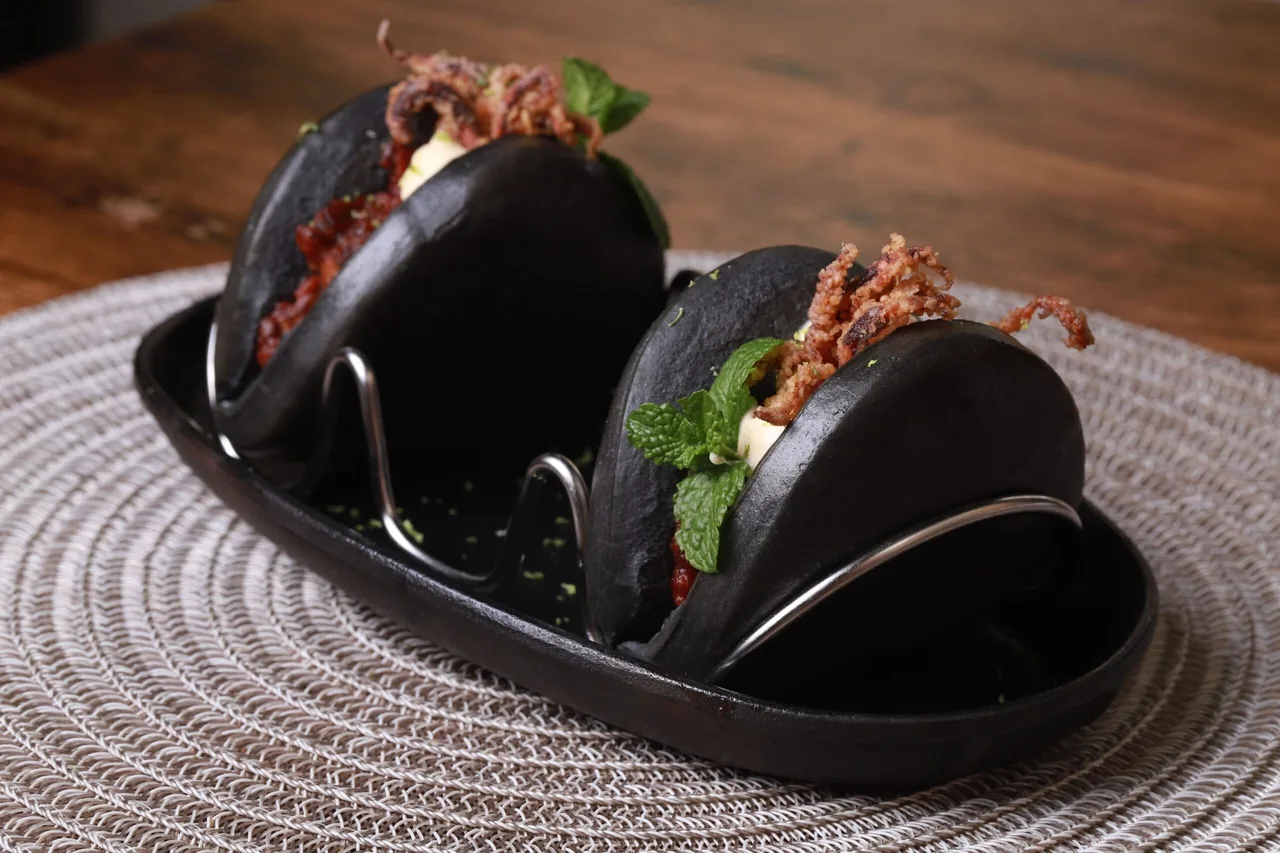 Two black buns filled with crispy fried strands and fresh mint in a black serving dish