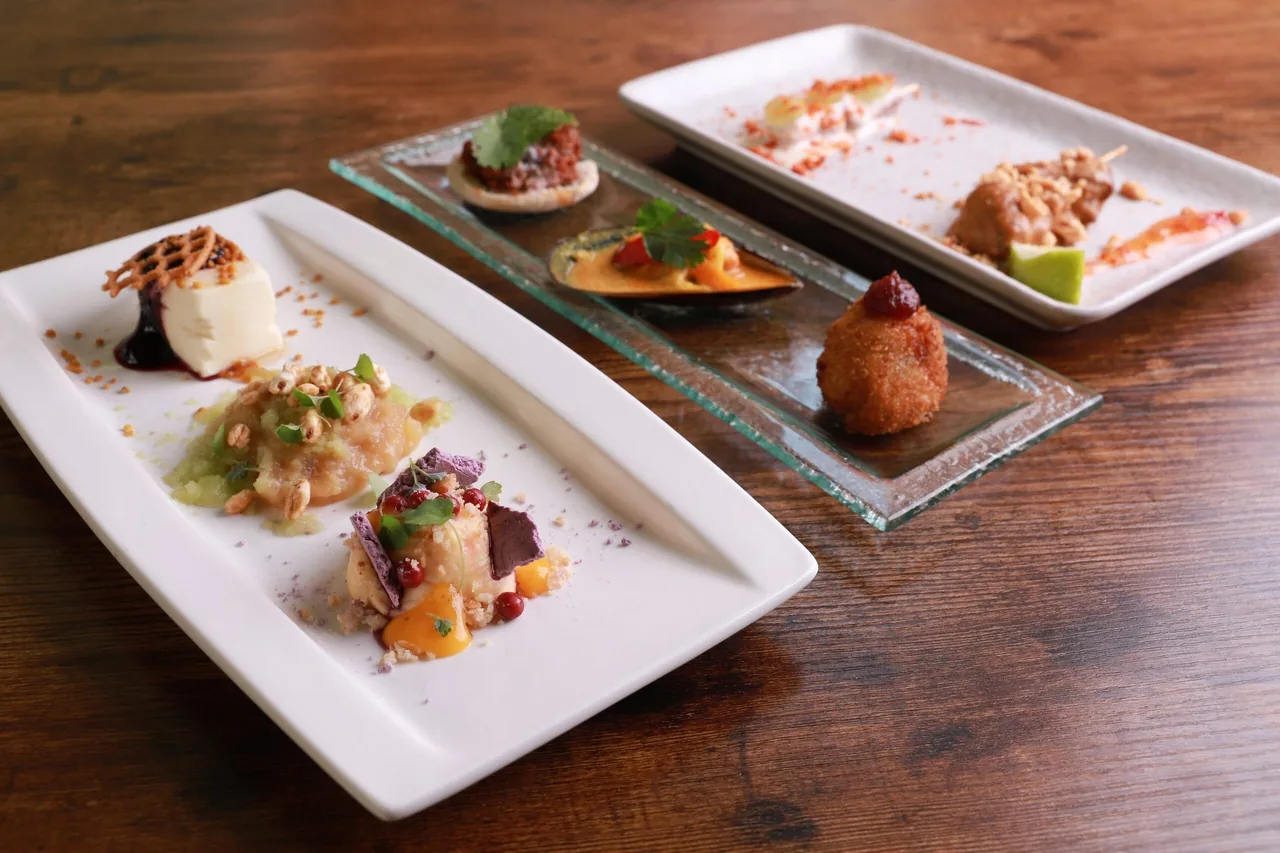 Three white rectangular plates of small composed dishes on a wooden table