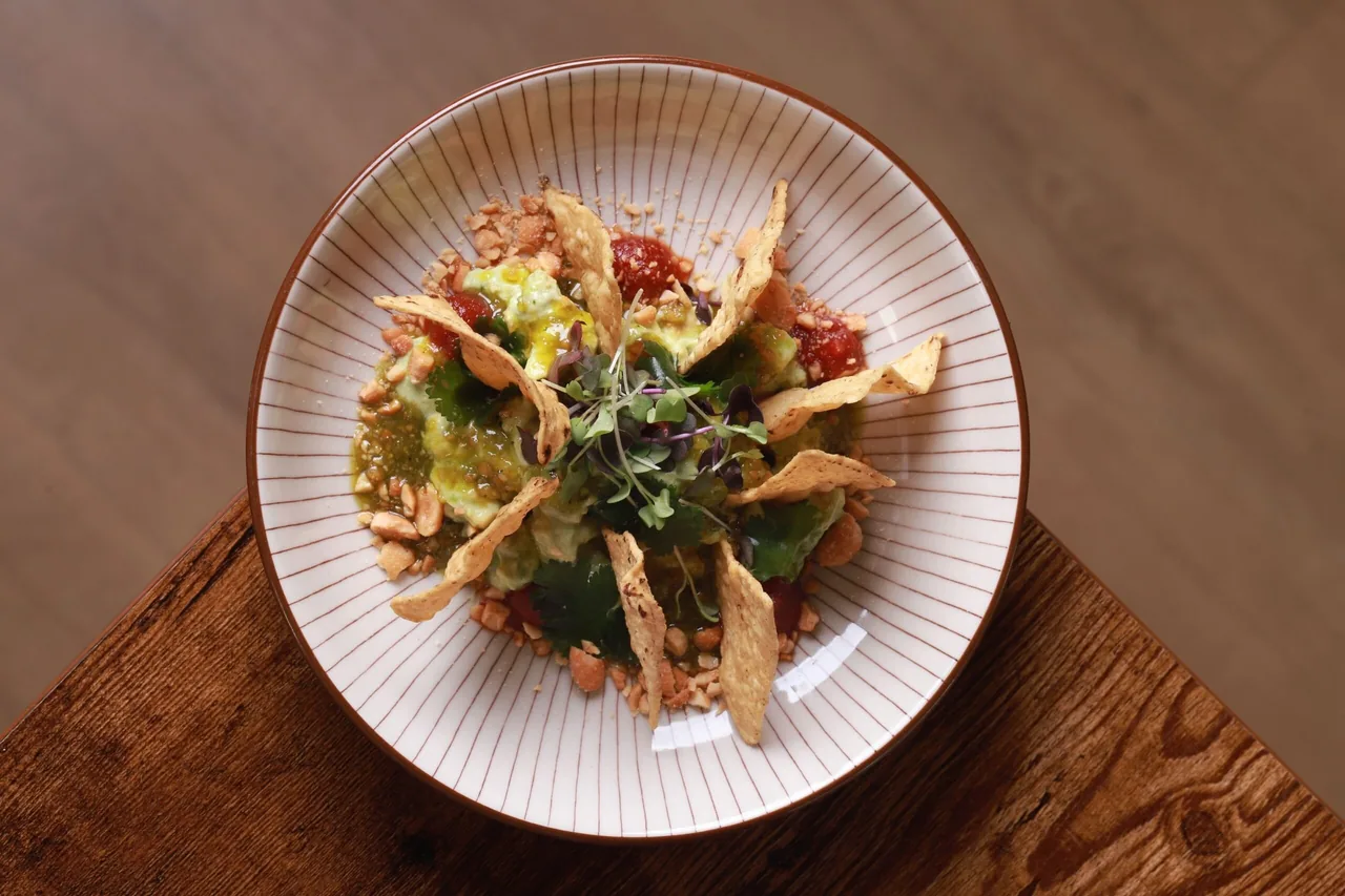 A round plate of a leafy salad with crispy toppings on a wooden table