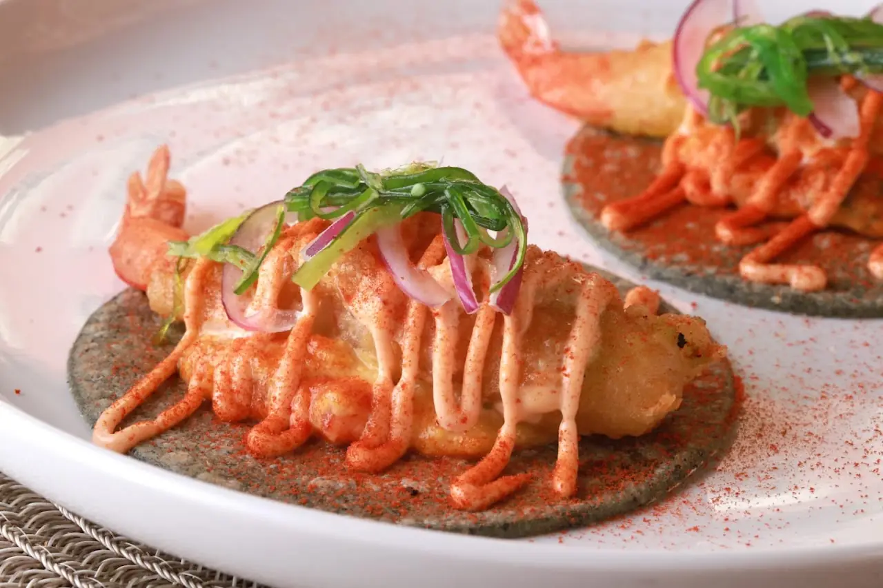 Two blue-corn tostadas topped with shrimp, pickled red onion, and a drizzle of spicy sauce.