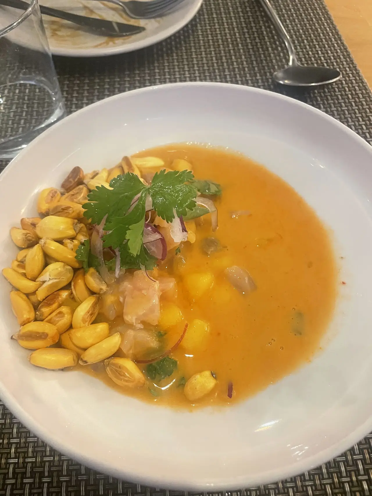 A bowl of yellow soup with corn kernels and fresh herbs
