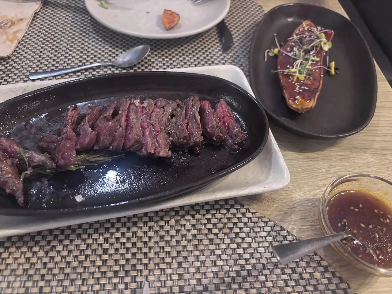 Sliced grilled steak on a sizzling black plate with a small dish of sauce