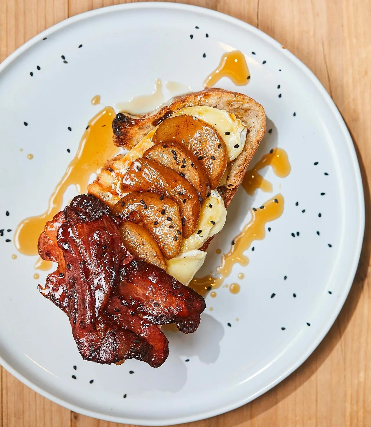 French toast topped with sliced fruit, maple syrup and crispy bacon on a white plate