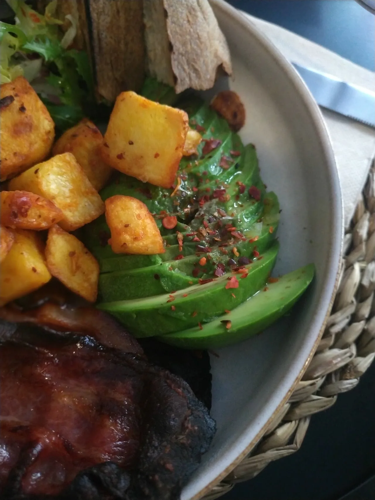 A plate of roasted potatoes with avocado slices and a piece of meat