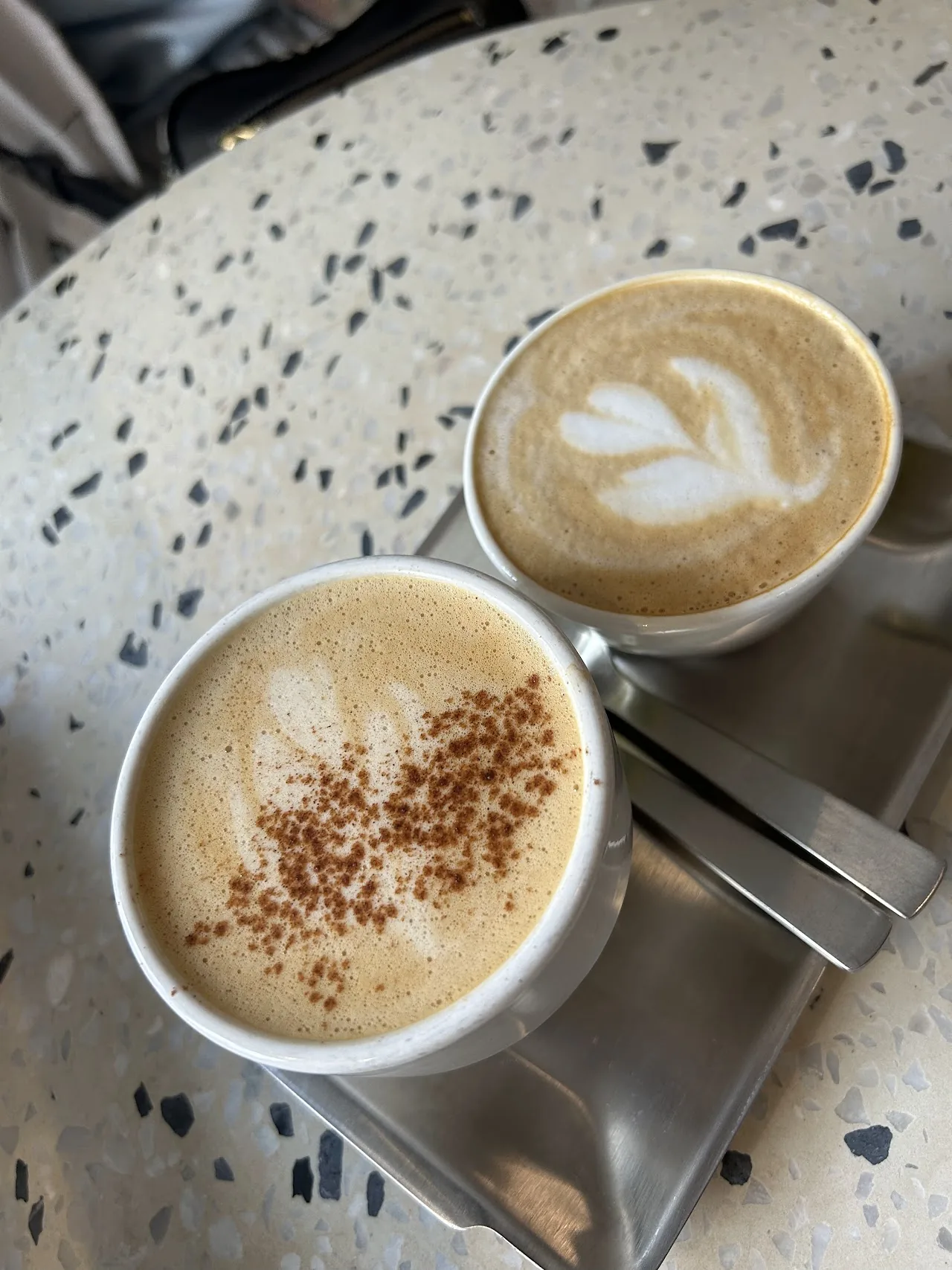 Two coffee drinks with latte art on a marble table