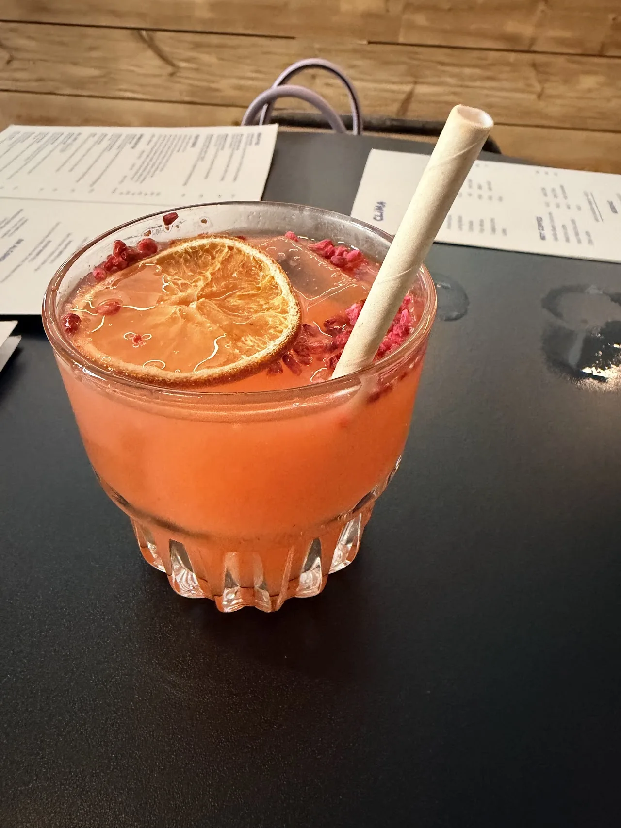 An orange cocktail garnished with a dried orange slice and pomegranate seeds