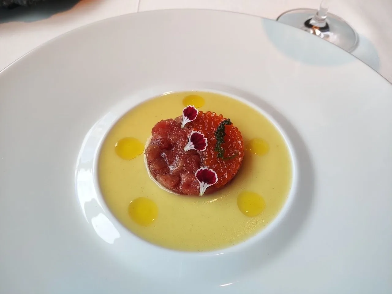 A raw meat tartare topped with roe on a pale yellow sauce in a white bowl