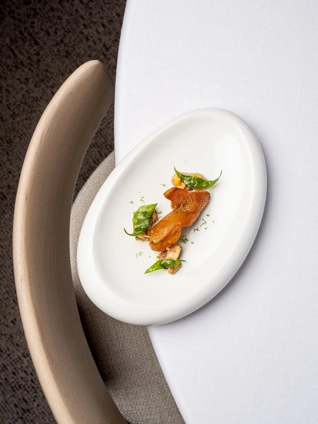 An oval white plate on a round table with a small orange and green garnished dish