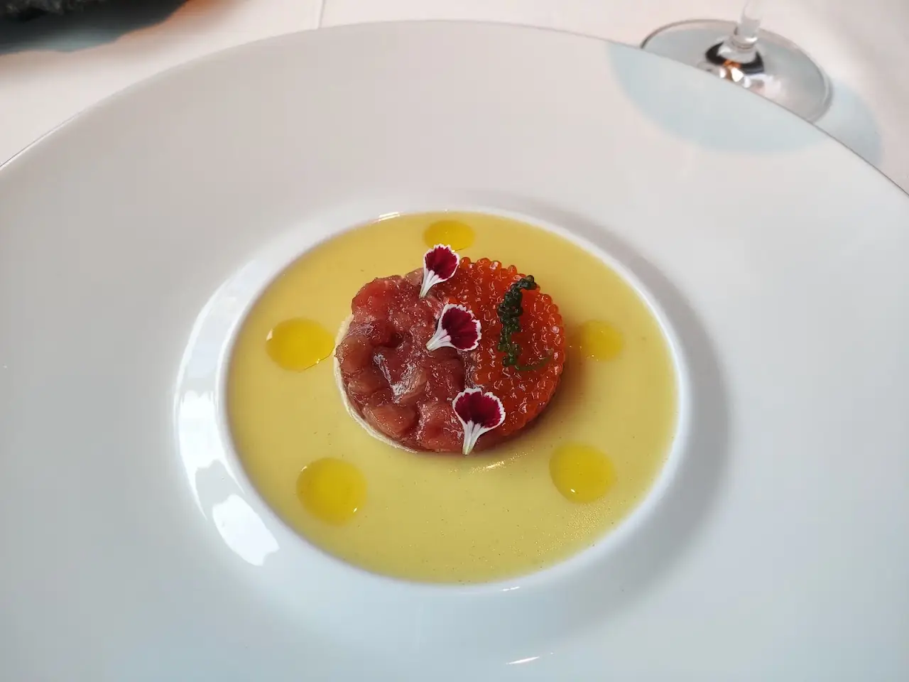 Diced red tartare topped with roe and flowers, set in a pool of yellow sauce on a wide white plate