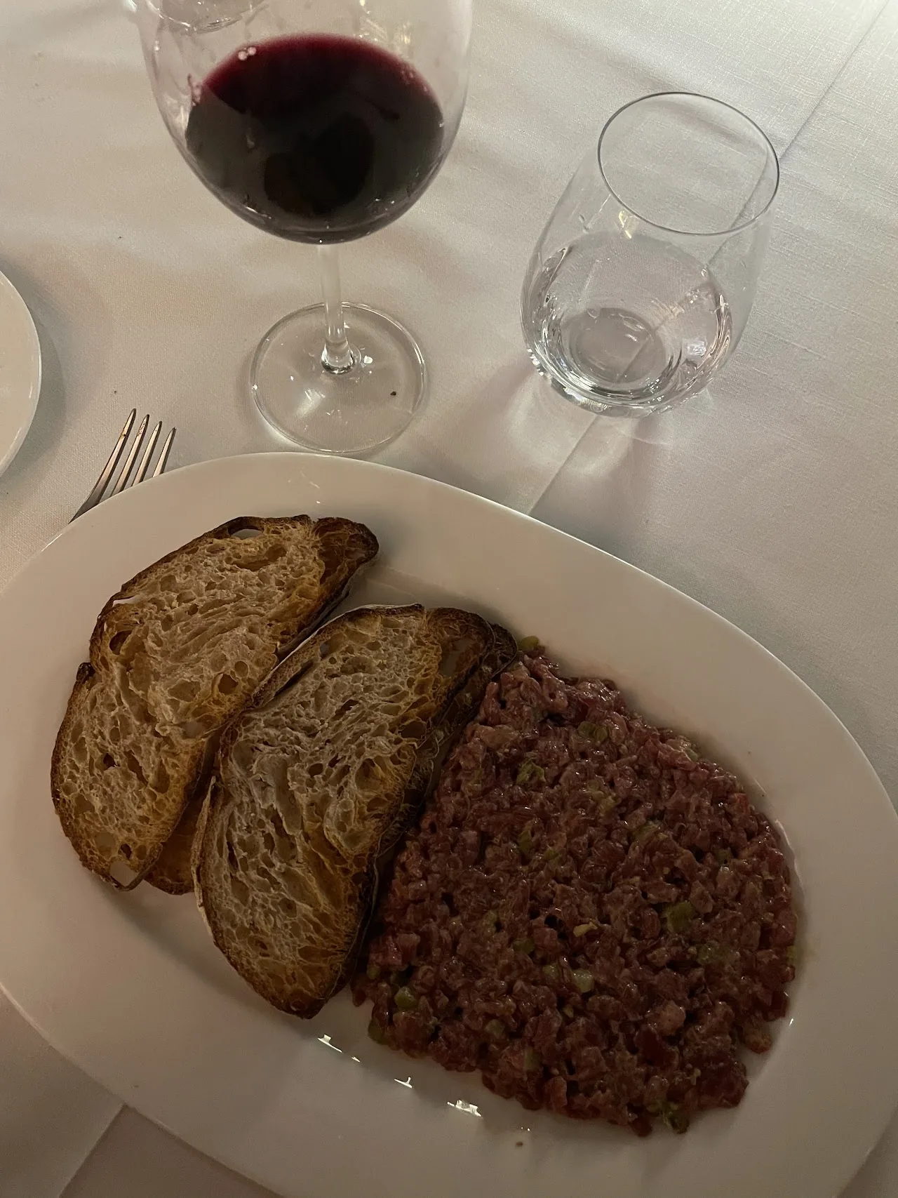 Toasted bread slices next to a scoop of steak tartare, with a glass of red wine