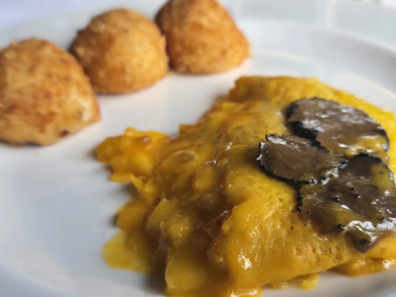 Three fried croquettes beside a portion of pasta topped with shaved truffle