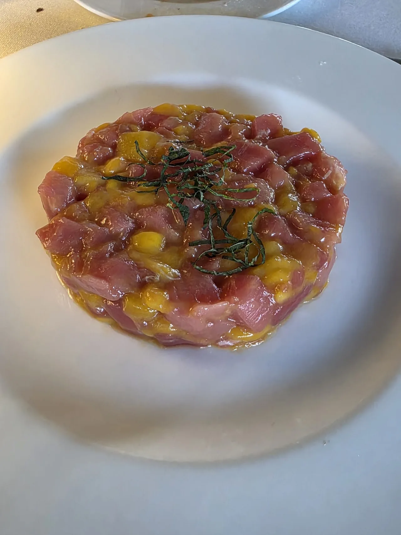 Tuna tartare topped with diced mango and herbs on a white plate