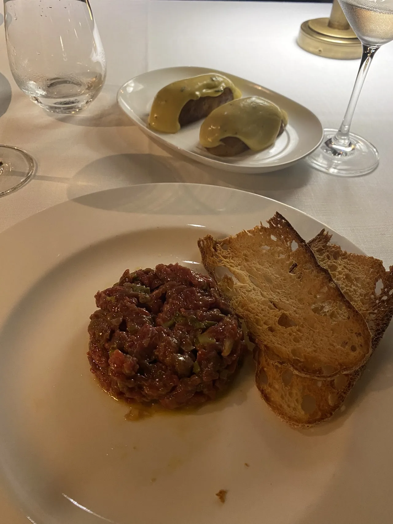A tasting plate with two savory bites next to a plate of tartare and toast