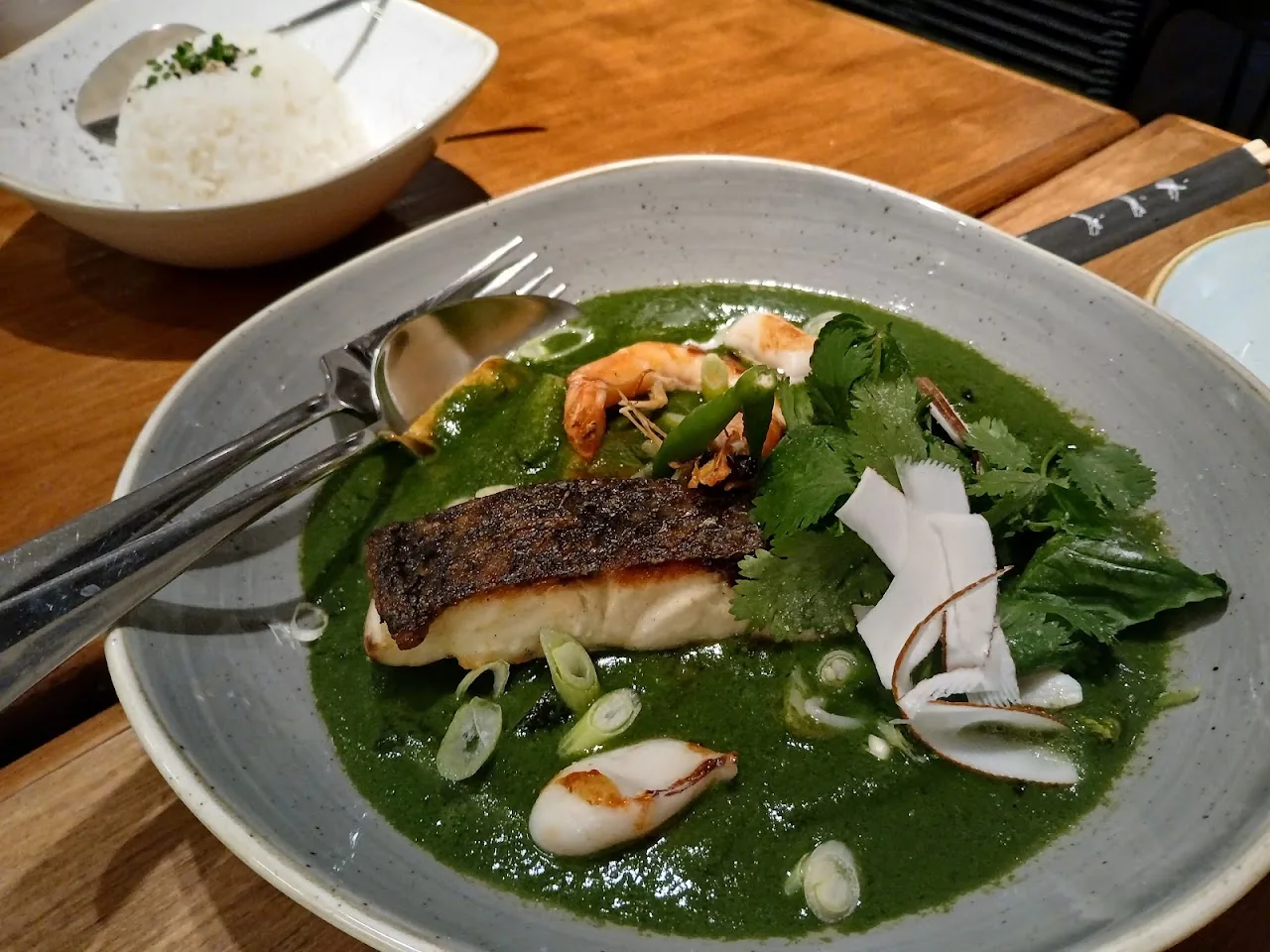 A piece of fish with crispy skin over greens in a green herb sauce