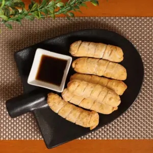 Five fried tequenos arranged on a black dish with a small square bowl of dark dipping sauce