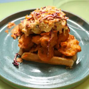 Fried chicken topped with slaw stacked on a waffle on a green plate
