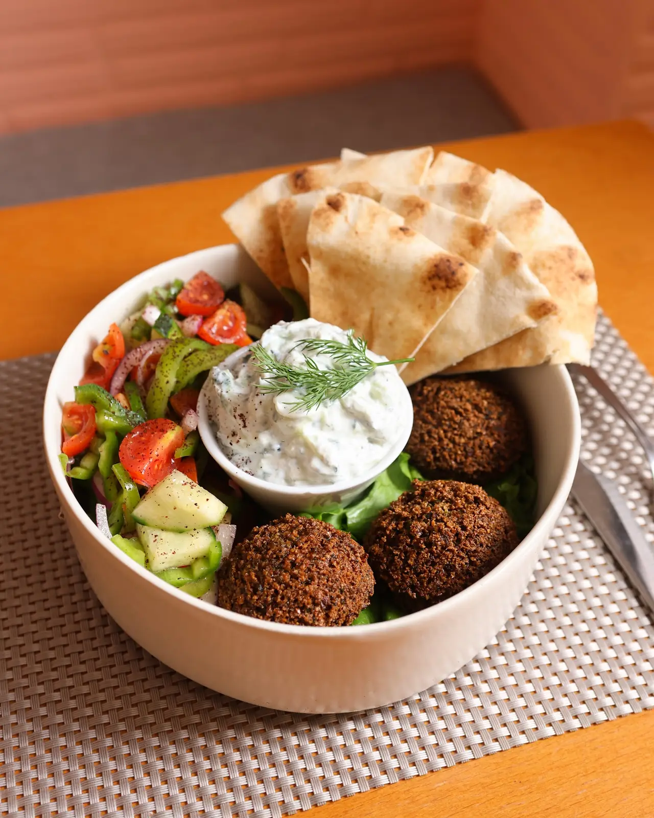 A bowl of falafel with pita bread, hummus, and a fresh salad.