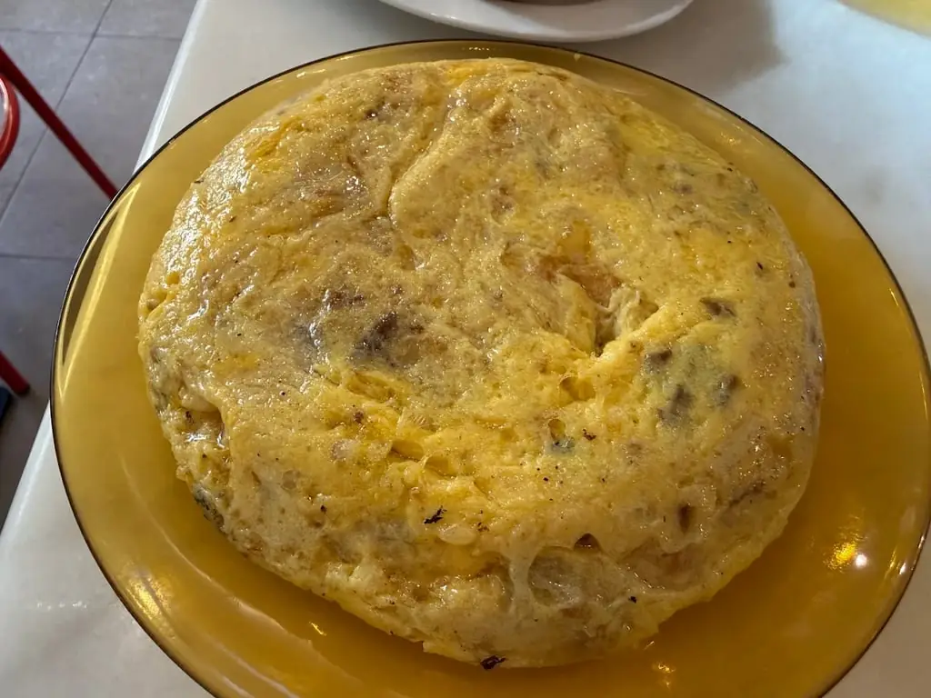 Round Spanish tortilla de patatas on a yellow plate, viewed from above, Colmado Carpanta