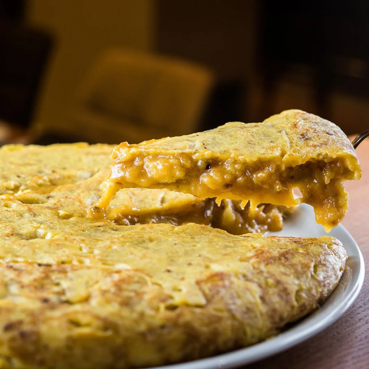 A wedge of potato omelette lifted from a whole one on a plate, showing the soft centre