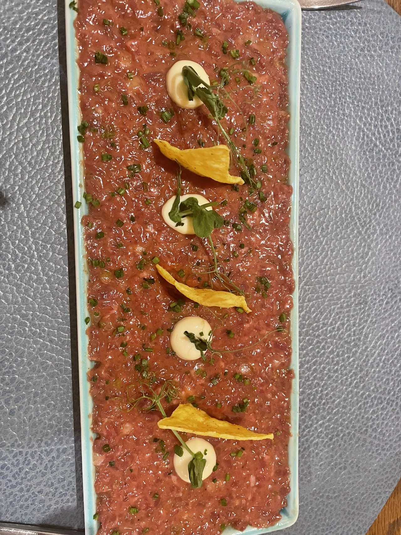 Thinly sliced beef tartare arranged with mango and herbs on a plate