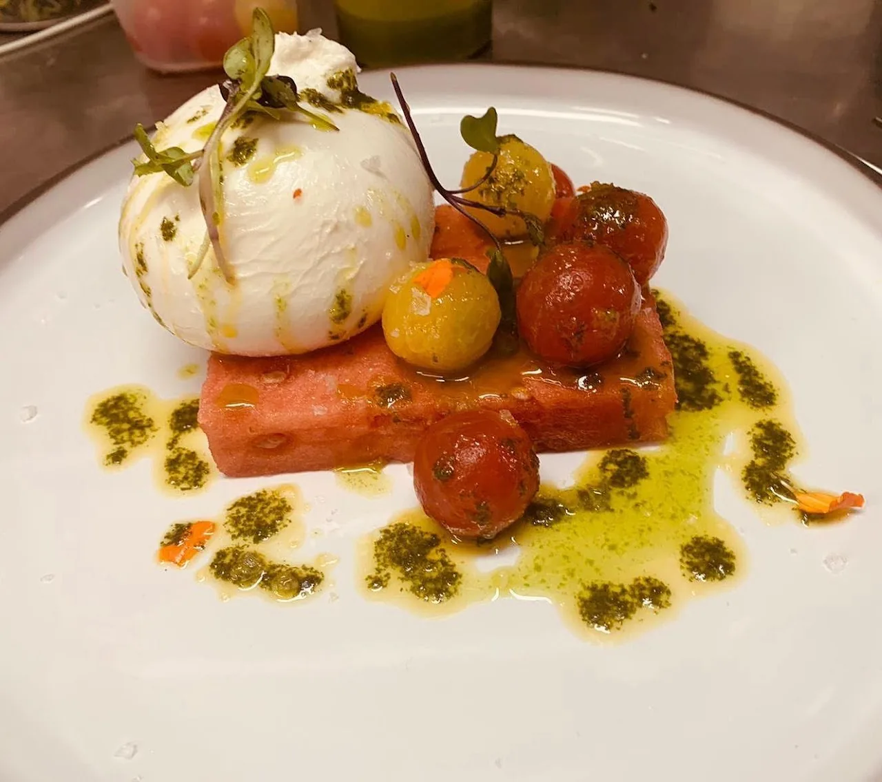 A burrata ball with sliced tomatoes, watermelon, and cherry tomatoes drizzled with herb oil