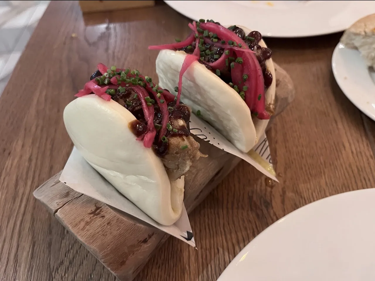 Two steamed bao buns filled with meat and topped with pickled red onion