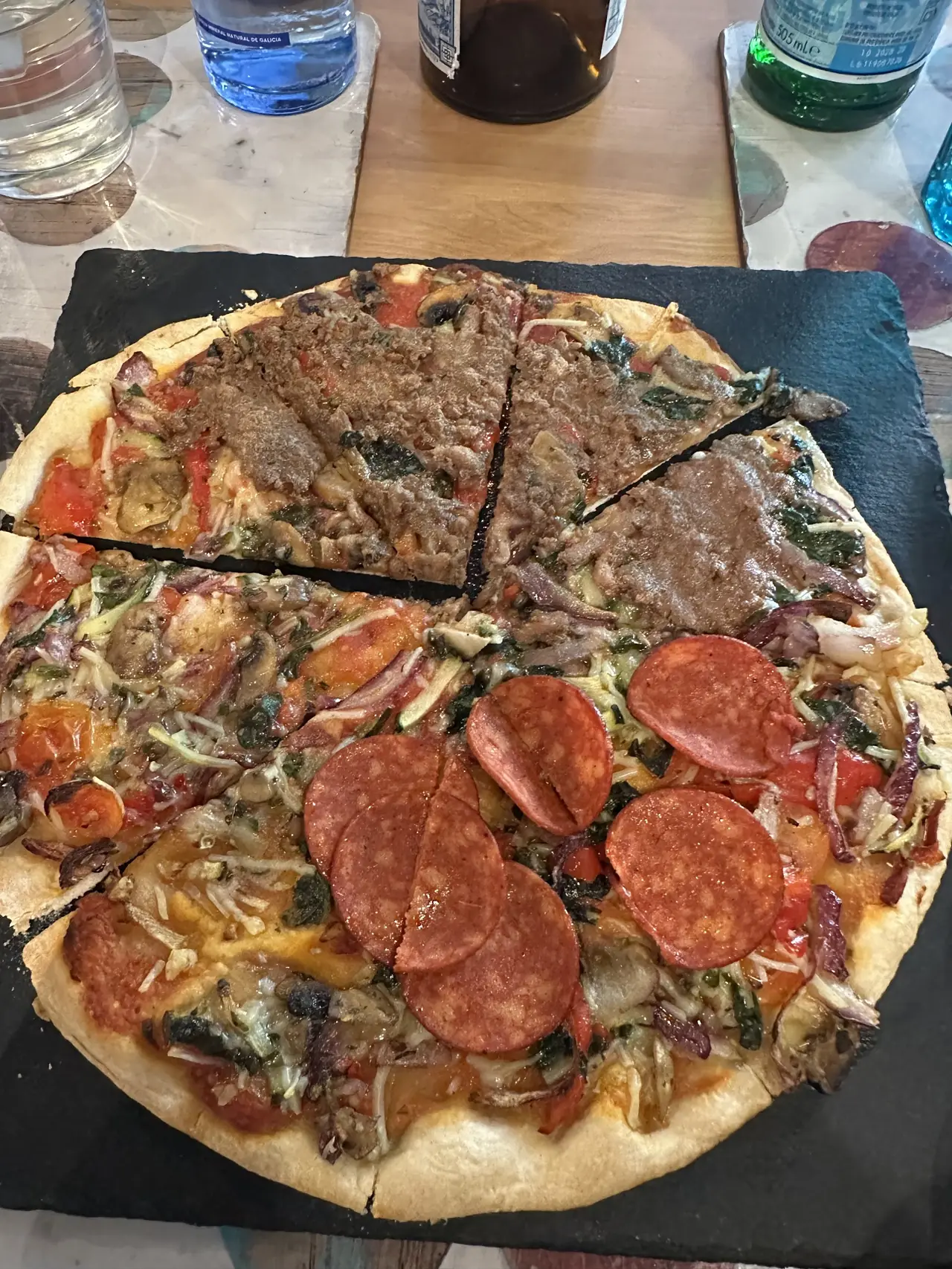 Sliced pizza topped with plant-based pepperoni and crumbled meat alternative on a slate board