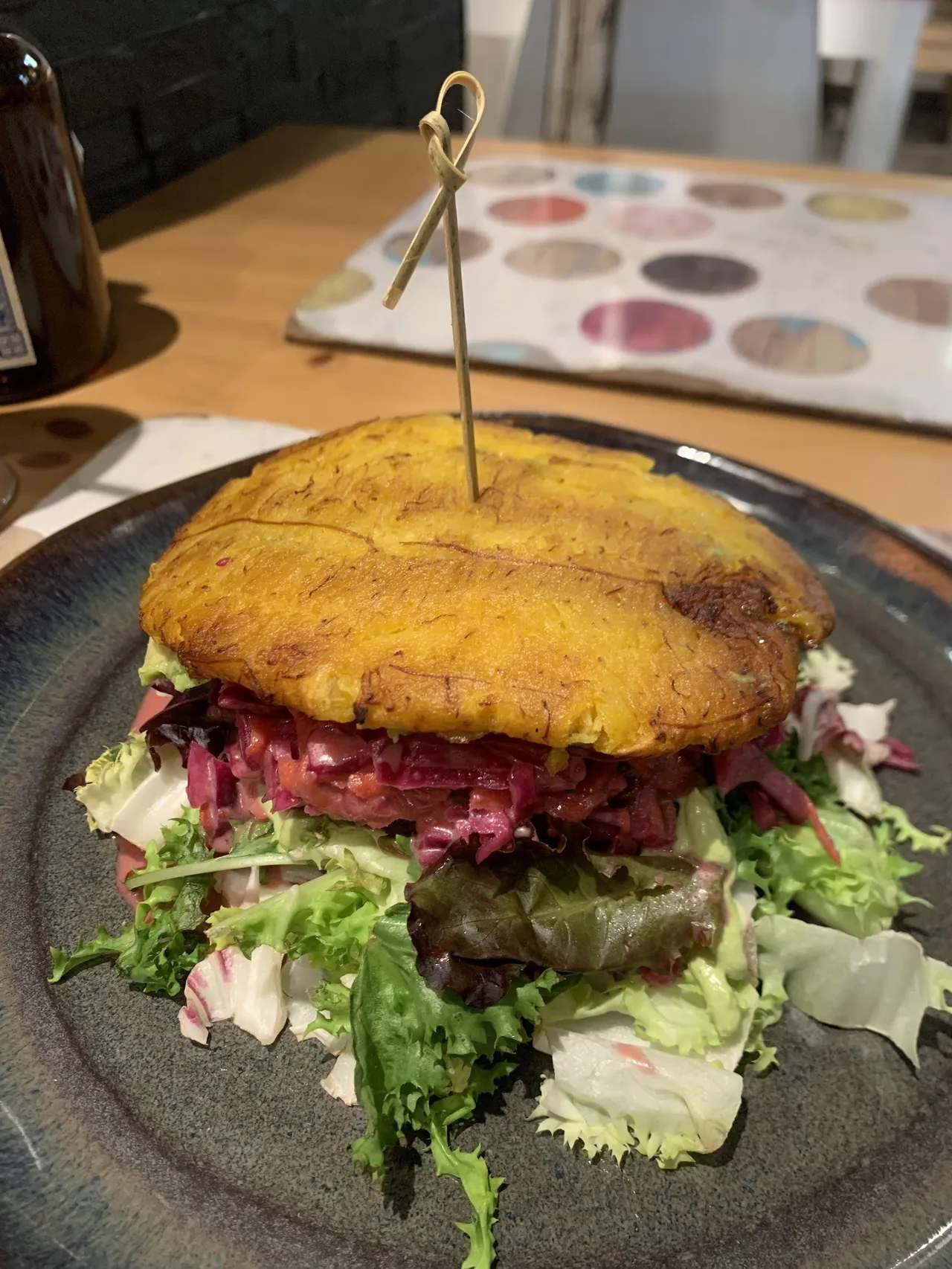 A golden bun-style burger with pink cabbage and salad leaves on a dark plate