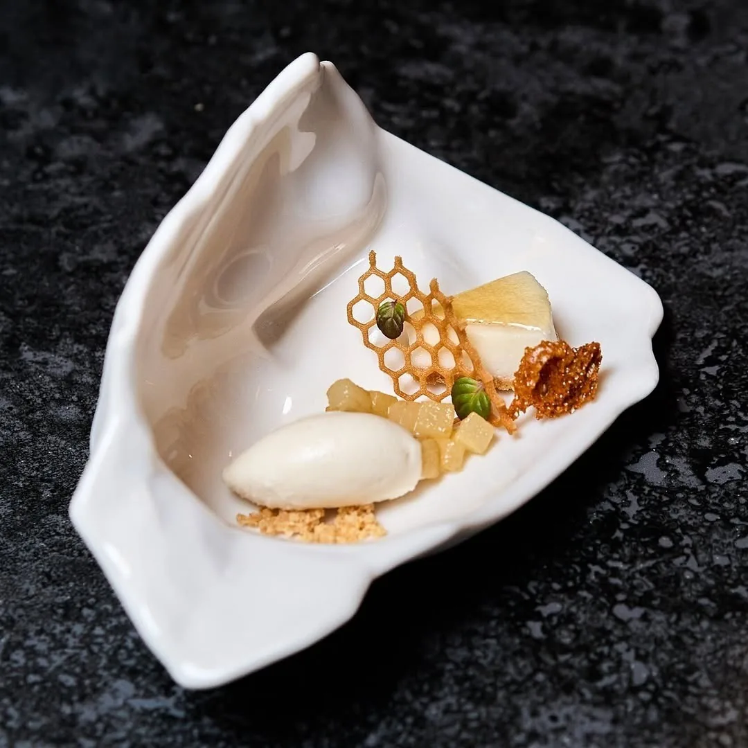 A dessert of ice cream and honeycomb served in a white shell-shaped dish on a dark surface