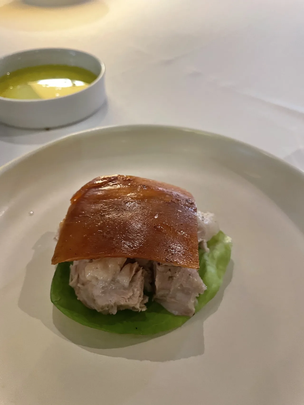 A piece of roast pork with a glossy crackling sheet on top, resting on a lettuce leaf on a white plate