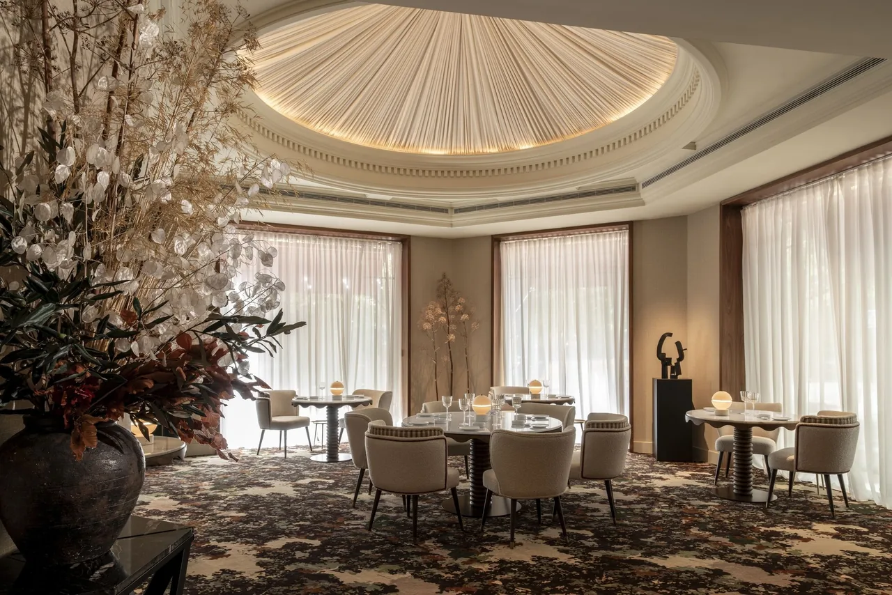 A round dining room with a domed ceiling, set tables, tall windows and a large floral arrangement