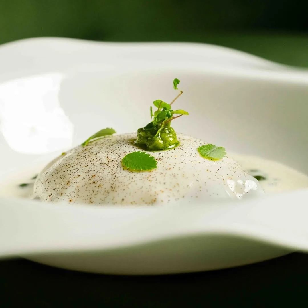 A white plate with a pale foam, small green leaves and a dusting of powder