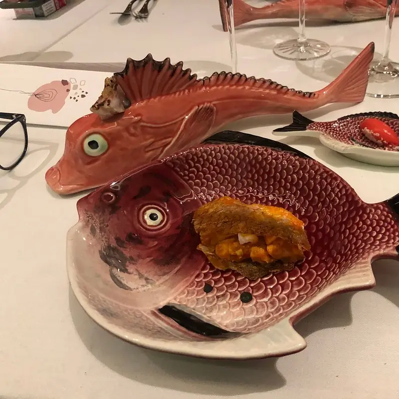 Fish-shaped ceramic serving dishes with small plated bites of seared fish and shellfish on table
