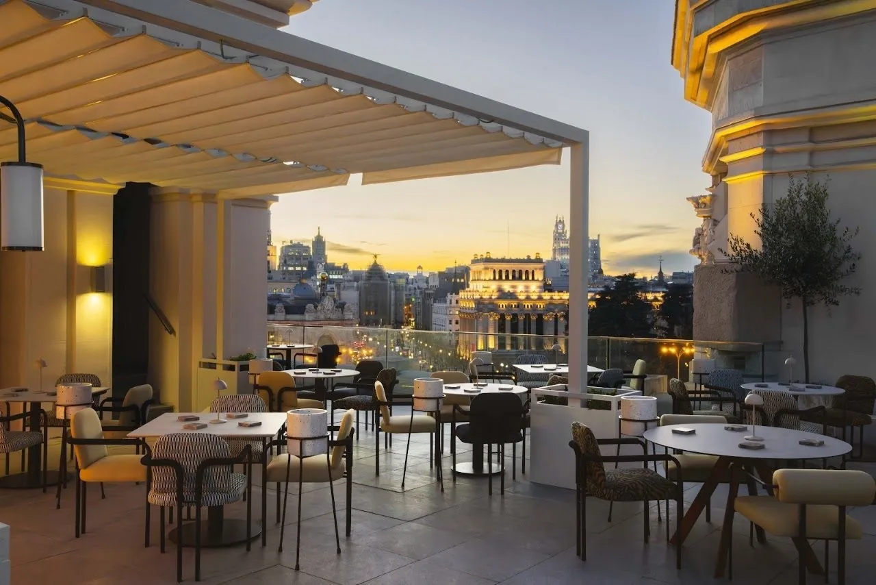A terrace with tables and chairs under a white canopy looking over Madrid at dusk